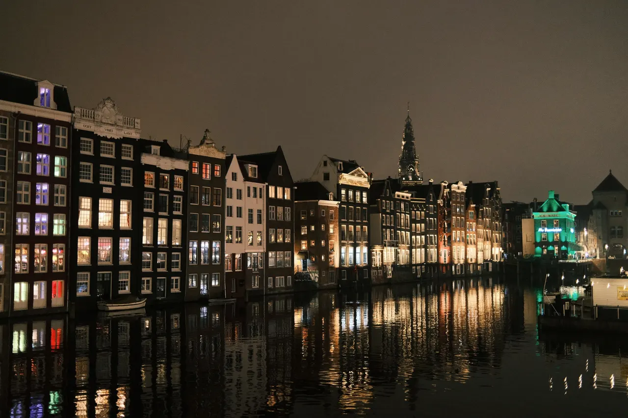 Amsterdam canal houses at night, their lit windows reflected in the still water