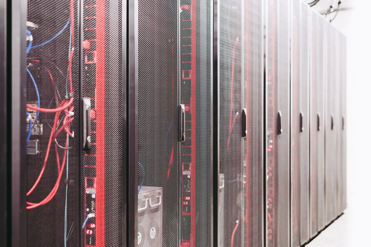 A row of dark server cabinets, one door open with red and blue cabling inside