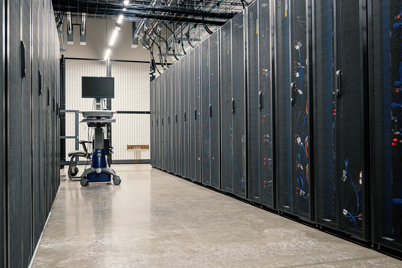 A long aisle between closed server cabinets under strip lighting, a monitor cart at the far end