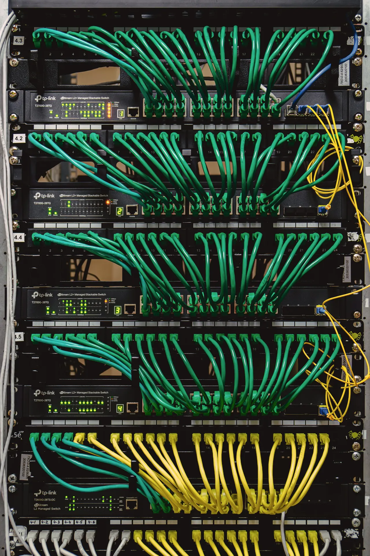 A rack of switches with green and teal patch leads fanned into each one